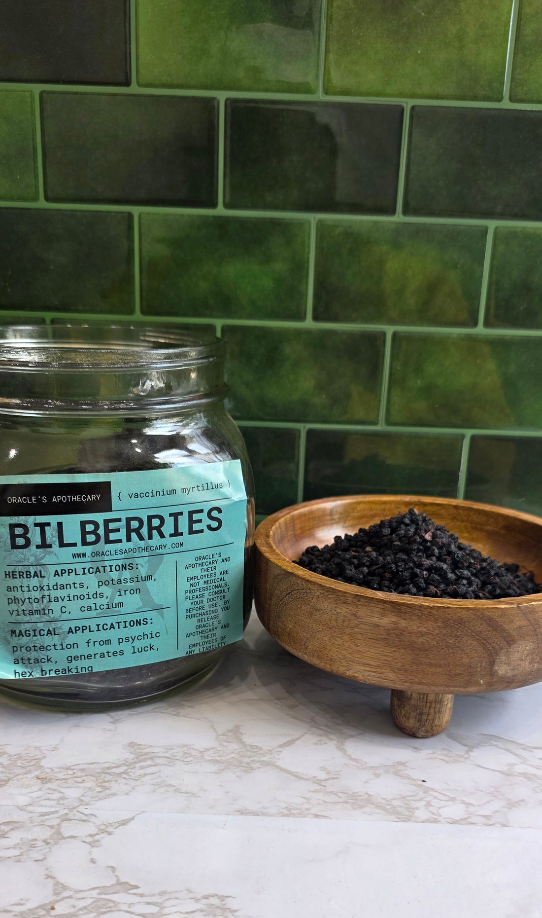 Bilberries in clear jar with label and in wood bowl on a marble counter top with green tile background