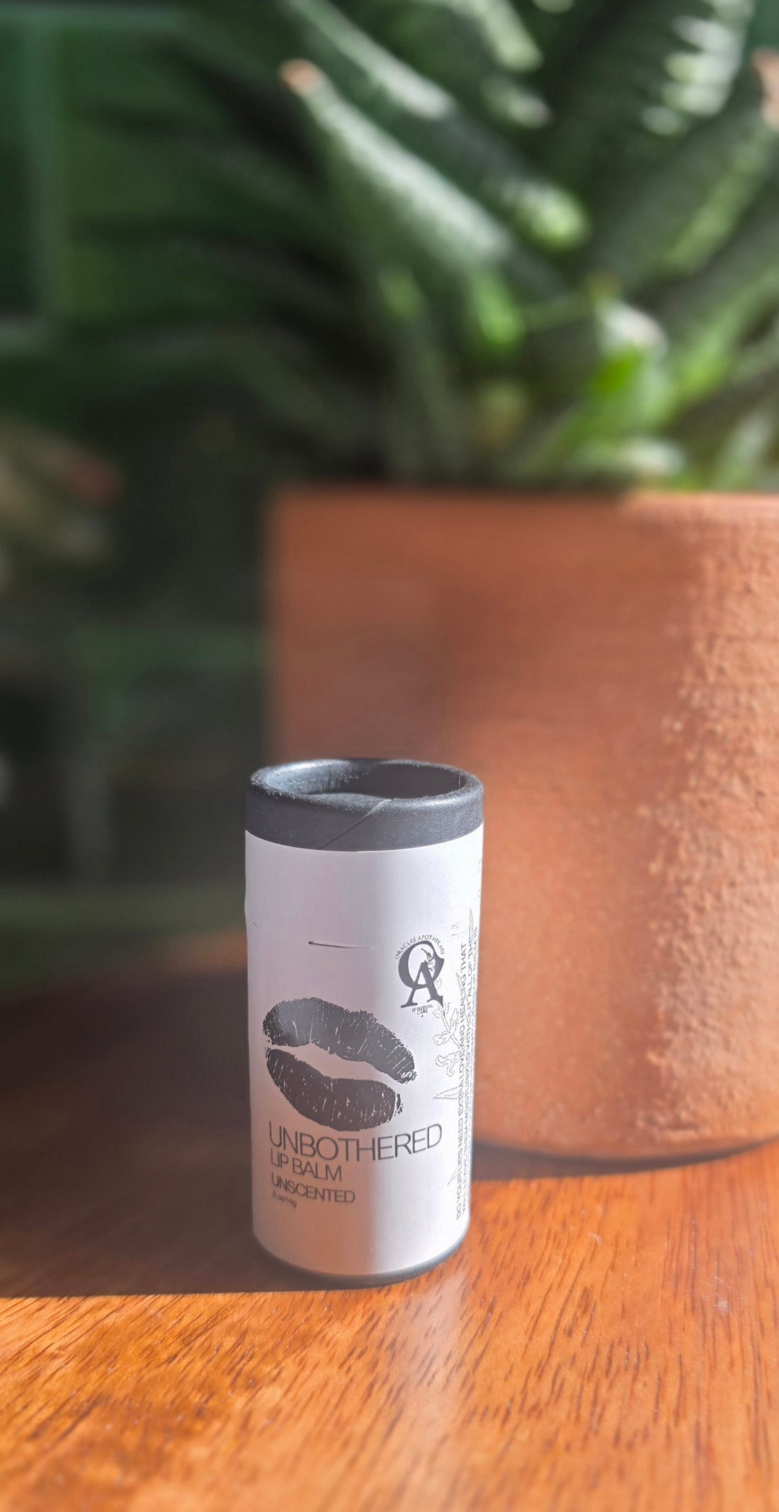 Black cylinder tube with black lid on a wooden surface with a blurred plant in the background
