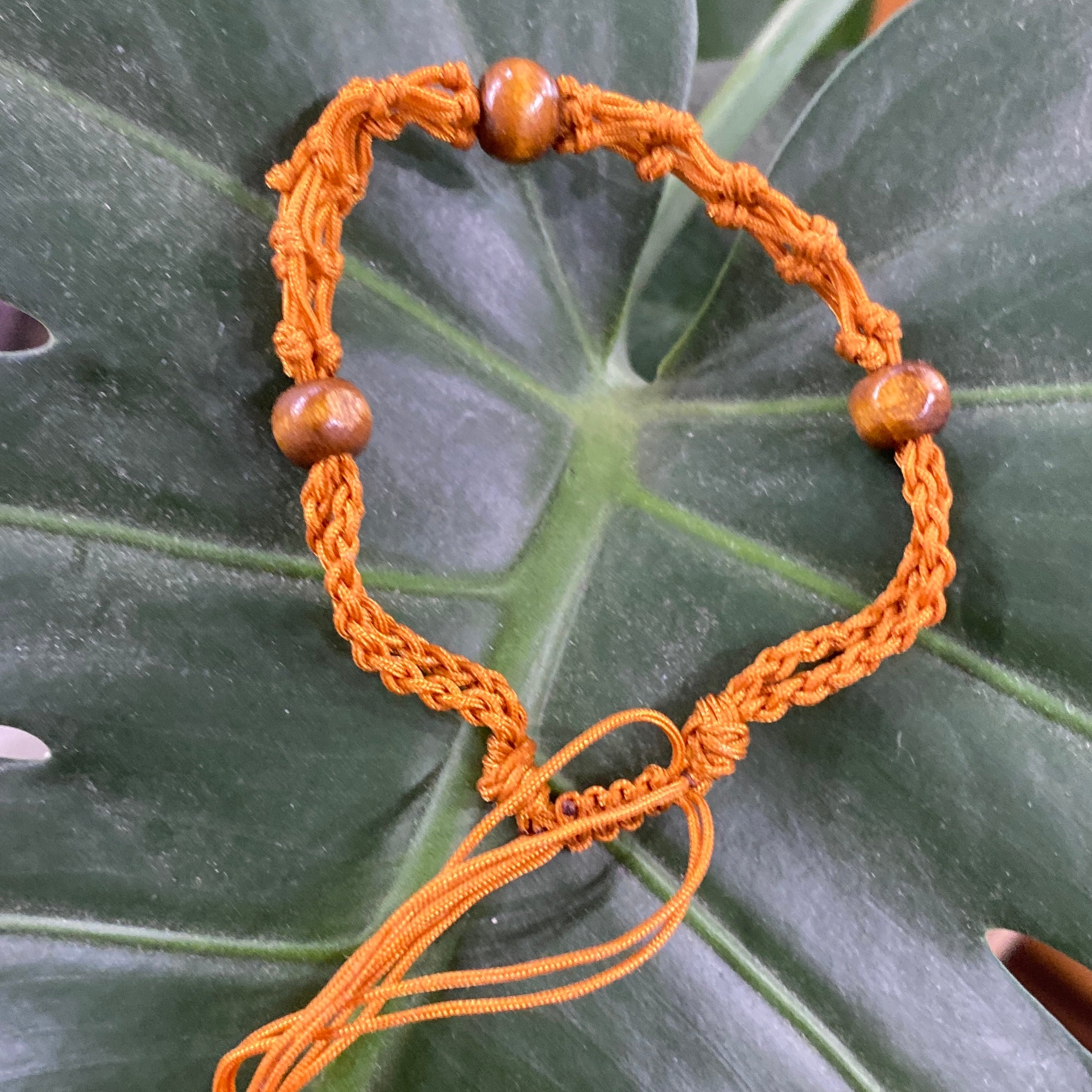 a tan threaded bracelet with 3 wooden beads braided into it.