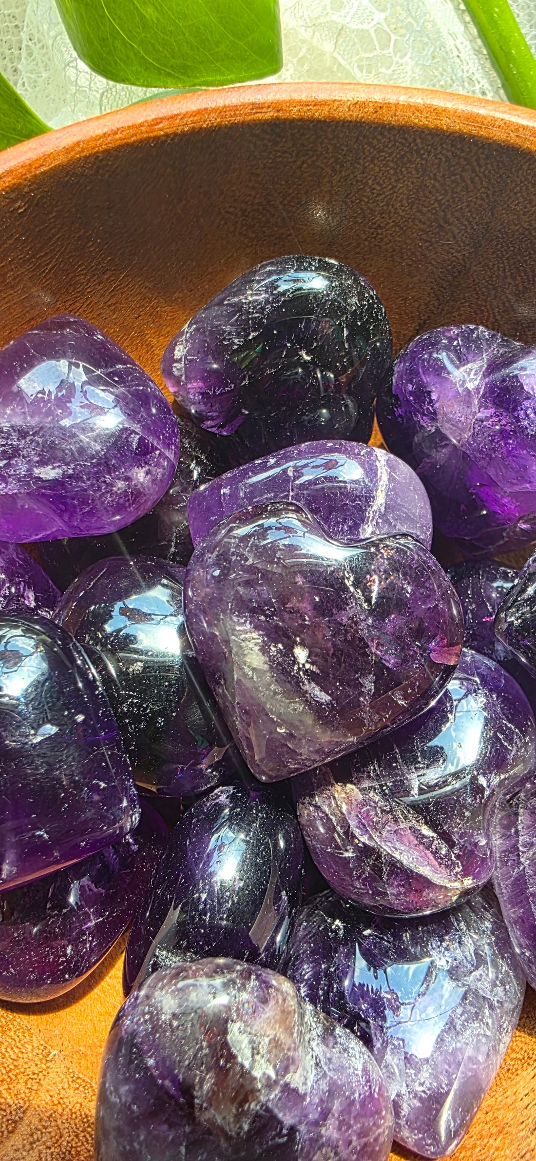 Amethyst crystals in a wooden bowl with green leaves in the background