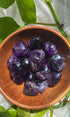 Amethyst crystals in a wooden bowl with green leaves in the background