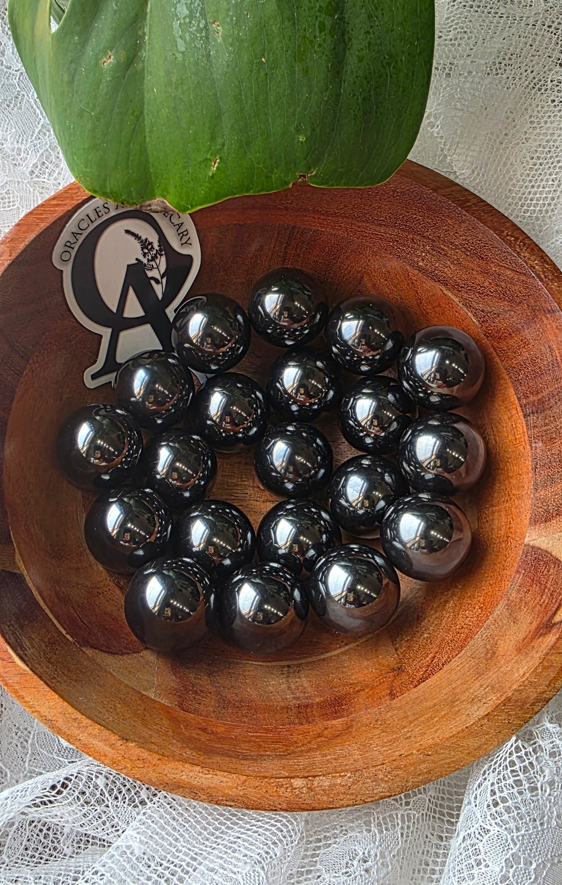 Black marbles in a wooden bowl with a brand logo on a white lace background