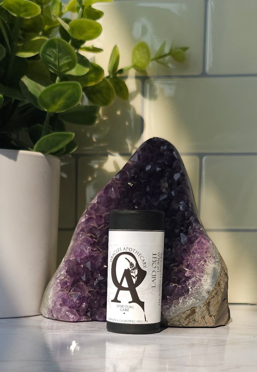 Laid Out Lip Balm in-front of a chunk of amethyst crystal