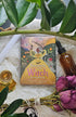 Seasons of the Witch: Litha Oracle deck lying next to roses and a tincture