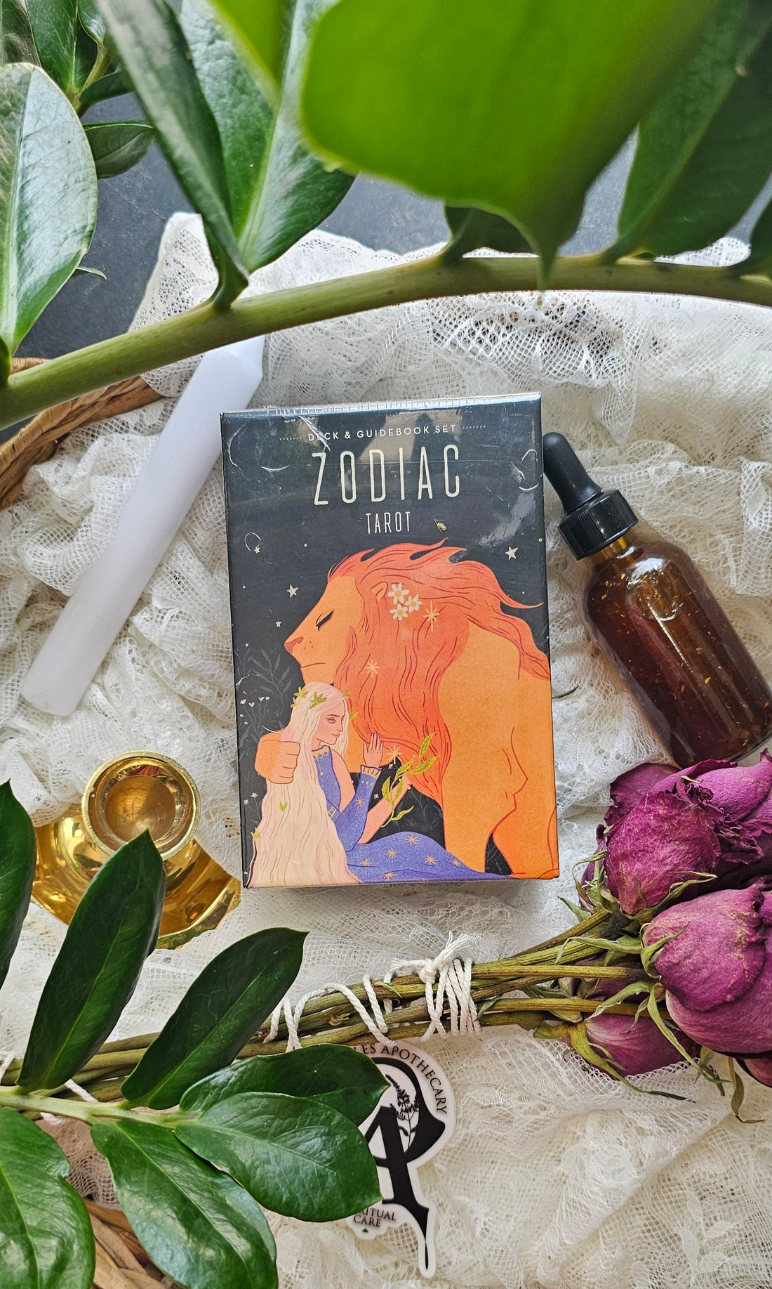 Zodiac Tarot Deck & Book Set lying next to roses and a tincture