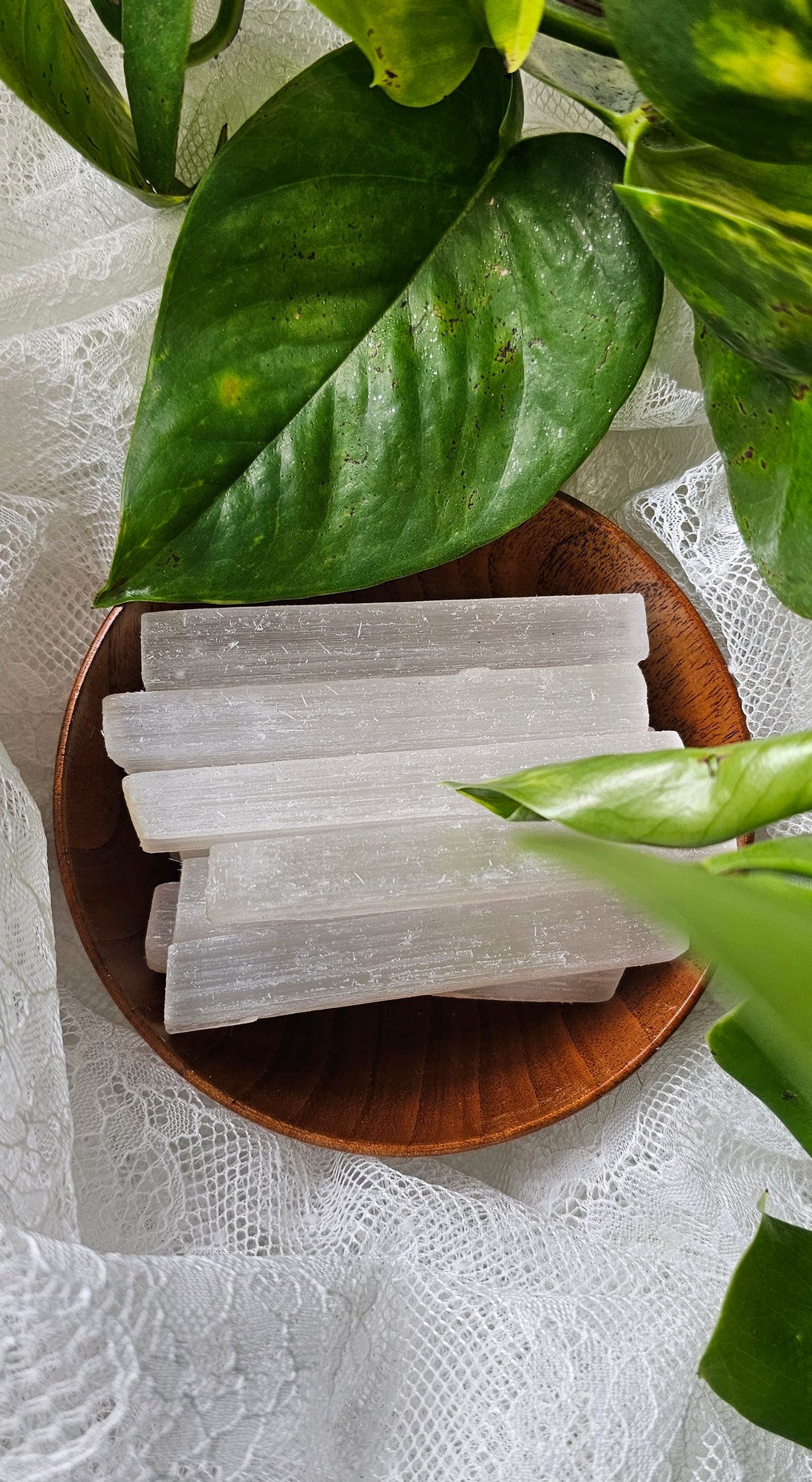 Selenite in a wood bowl surrounded by plants and lace