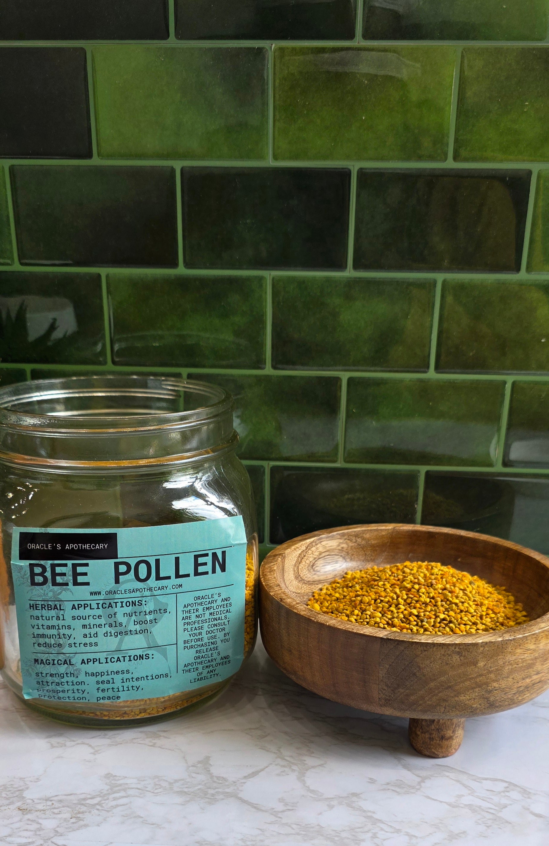 Bee Pollen in clear jar with label and in wood bowl on a marble counter top with green tile background 
