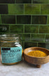 Bee Pollen in clear jar with label and in wood bowl on a marble counter top with green tile background 