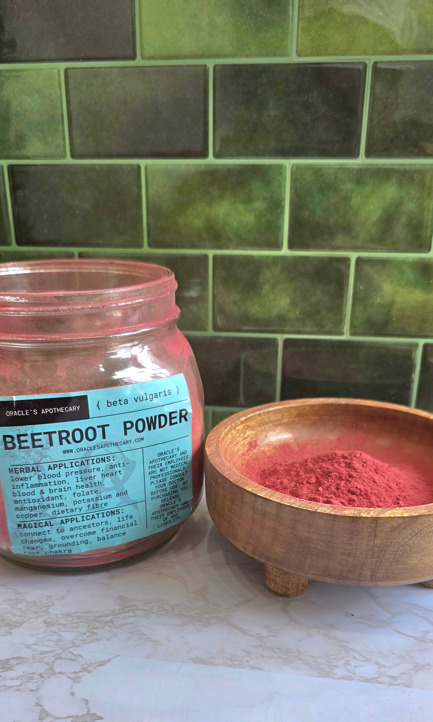 Organic Beetroot Powder in clear jar with label and in wood bowl on a marble counter top with green tile background 