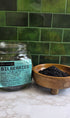 Bilberries in clear jar with label and in wood bowl on a marble counter top with green tile background 
