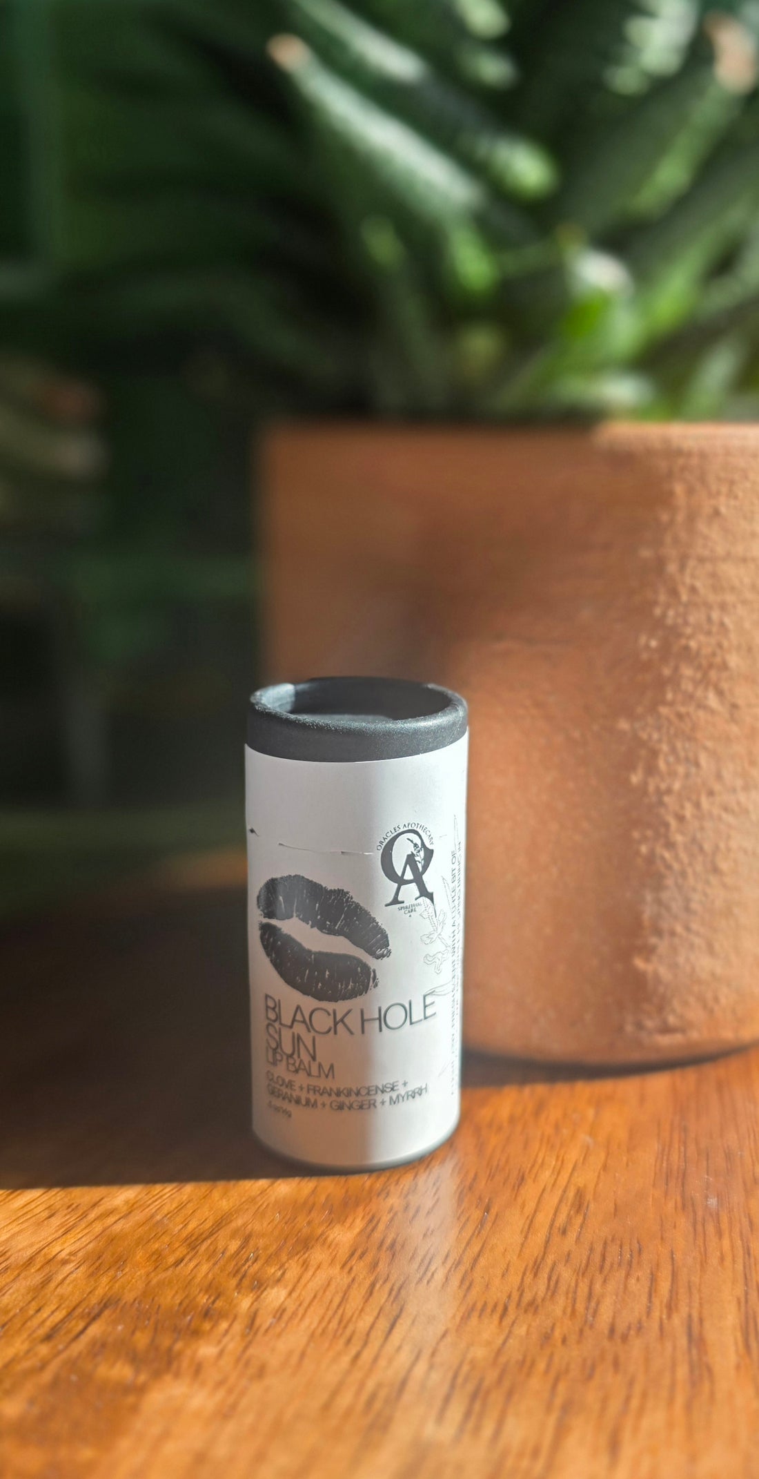 White cylindrical container with black lid on a wooden surface, blurred green plant in the background