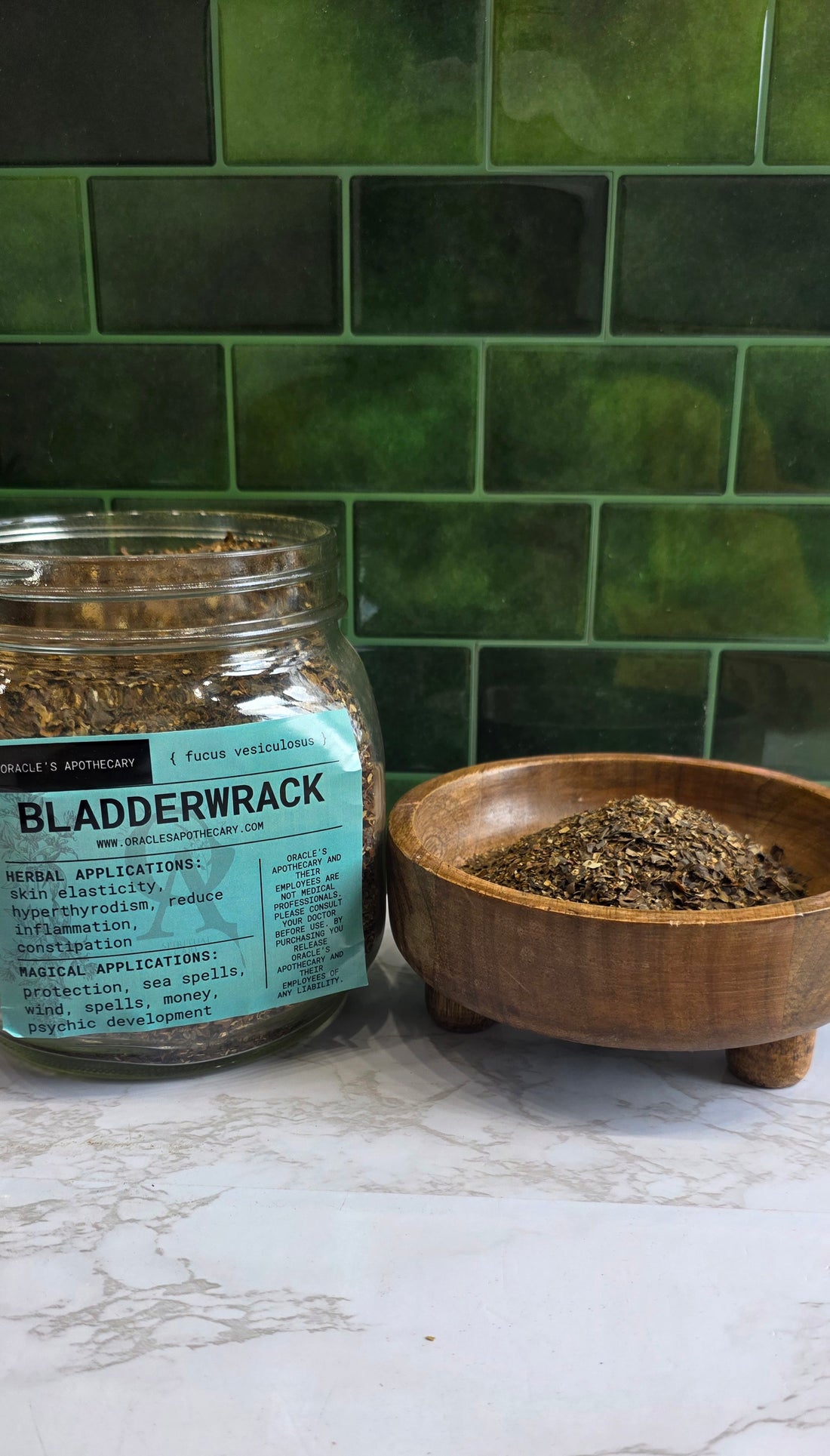 Bladderwrack in clear jar with label and in wood bowl on a marble counter top with green tile background 