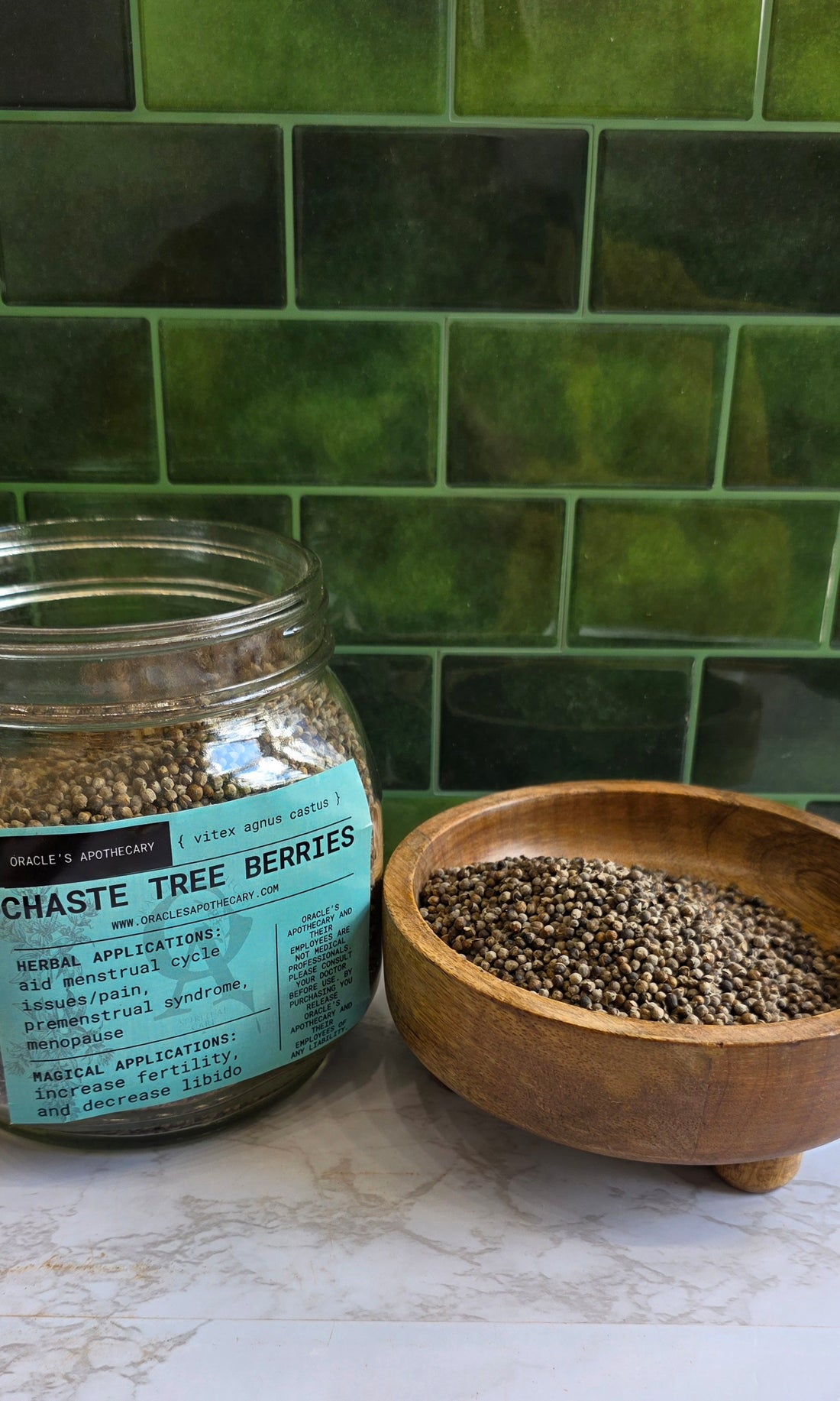 Chaste Tree Berries in clear jar with label and in wood bowl on a marble counter top with green tile background