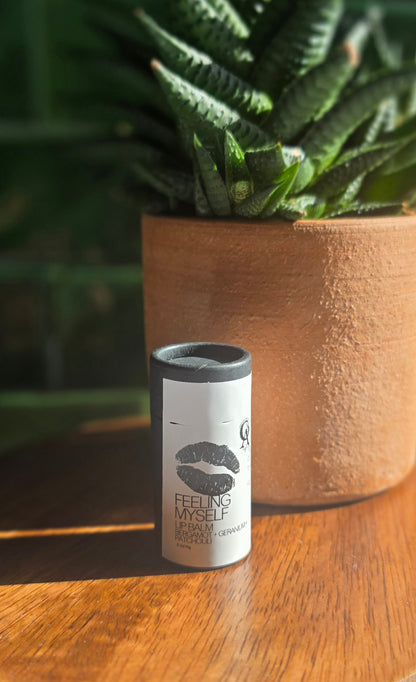 White label on black tube with black text and a black lid on a wooden surface with a plant in the background