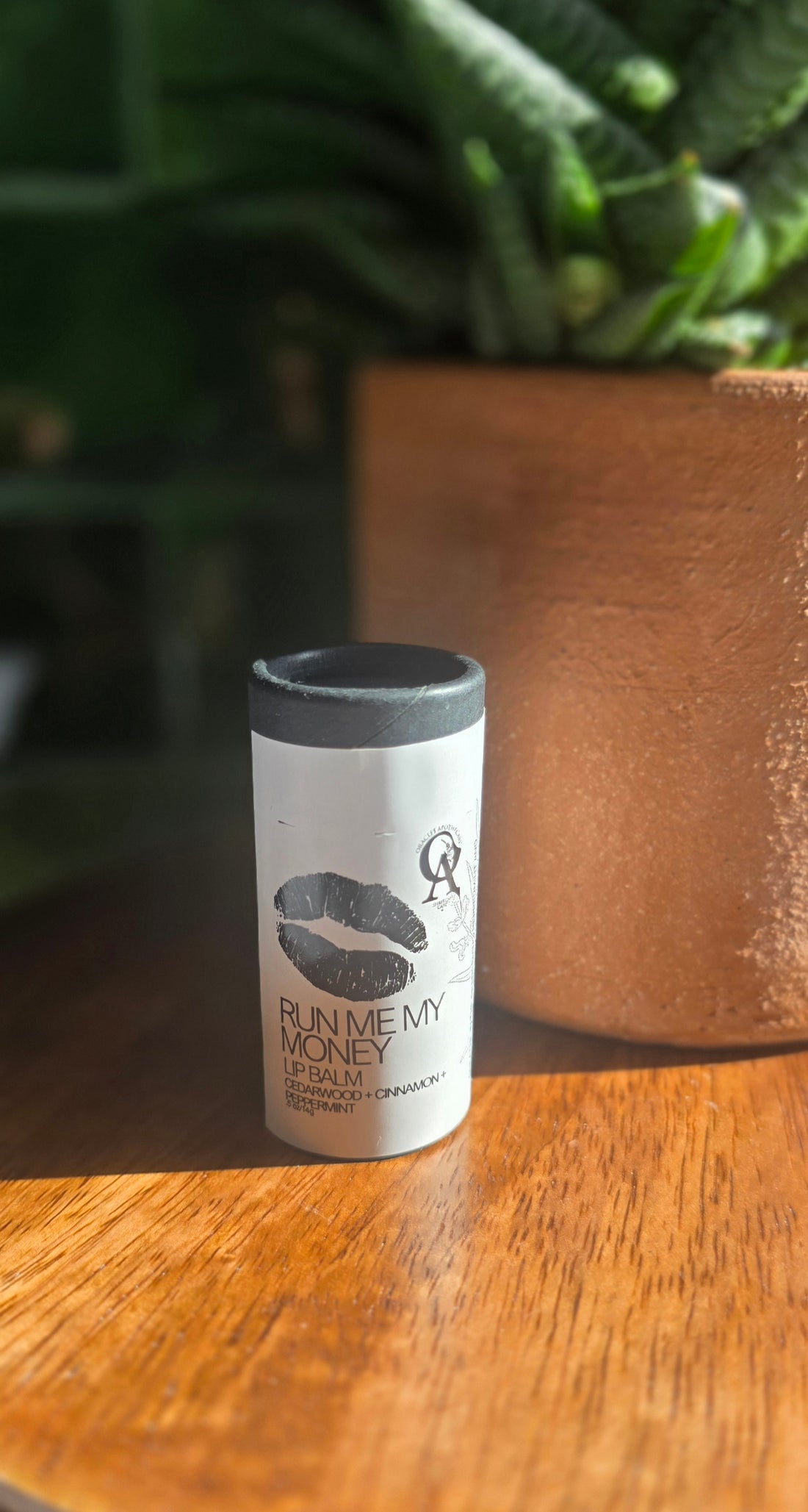 Small cylindrical container with a black lid on a wooden surface with a blurred green plant in the background