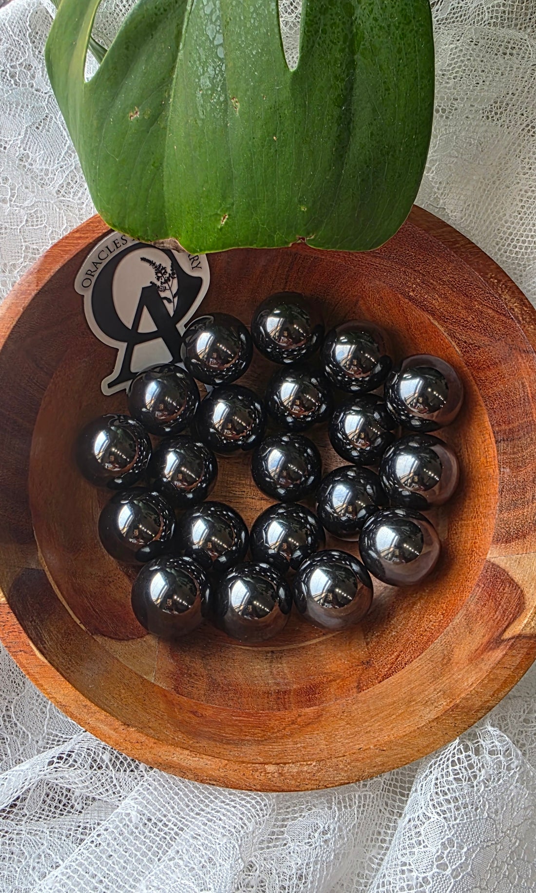 Wooden bowl with black spherical objects and a green leaf on a white lace background