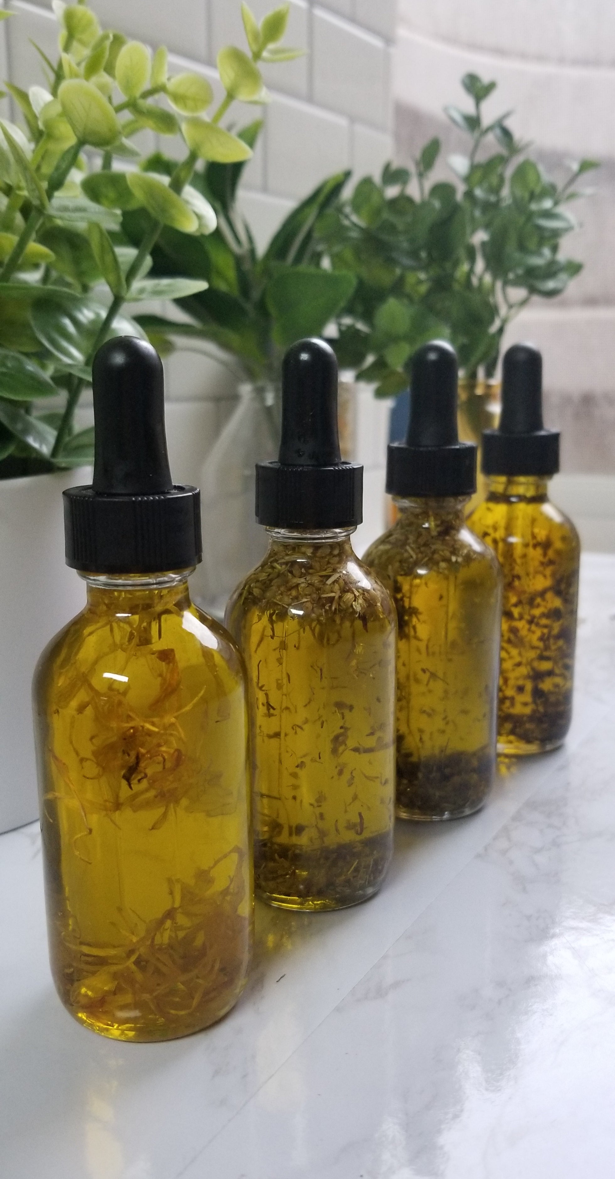 four glass dropper bottles filled with herbs and oil